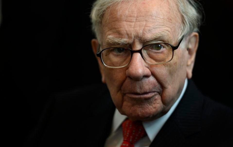Potret close-up Warren Buffett, investor legendaris, mengenakan jas hitam, kemeja putih, dan dasi merah bermotif dengan ekspresi serius dan bijaksana.